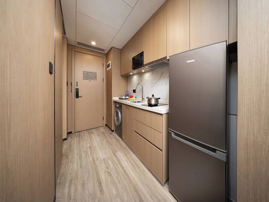A modern kitchen with wooden cabinets, a stainless steel refrigerator, a microwave, and a washing machine.