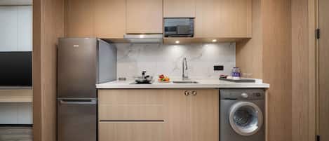 A compact kitchen with wooden cabinets, a stainless steel refrigerator, a microwave, a sink, and a built-in washing machine.