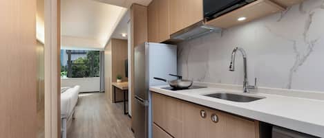 A modern kitchen with wooden cabinets, a stainless steel refrigerator, a microwave, and a sink.