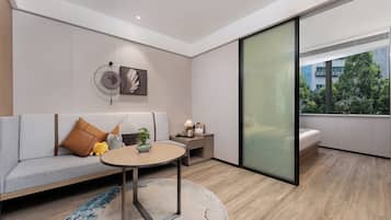 A modern living room with a sofa, a coffee table, a small side table, and a large window offering a view of greenery outside.
