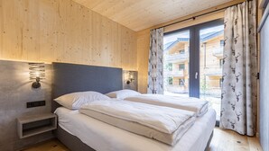 Camera da letto moderna con soffitto in legno, due letti con biancheria bianca, un comodino e un'ampia finestra con tende.