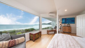 Un dormitorio con un ventanal grande con vistas al océano, una cama, un aparador y una estantería.