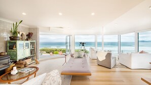 Un salón moderno con un amplio ventanal con vista al océano, un sofá, una mesa de centro y un aparador verde con objetos decorativos.