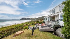 Una casa moderna con balcón de cristal con vistas a una playa y al océano.