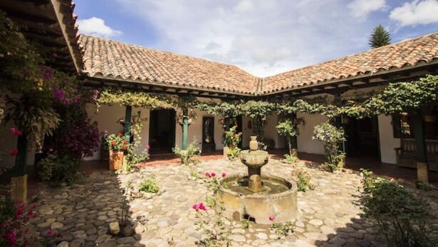 Un patio con una fuente de piedra, plantas en macetas y un tejado de azulejos.