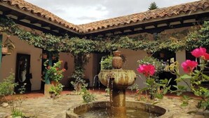Un patio con una fuente de piedra, plantas en macetas y un techo de tejas.