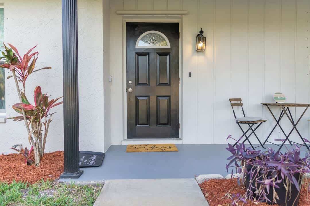 Une porte d’entrée avec un panneau foncé, un luminaire au-dessus, et une petite table avec des chaises sur le côté droit.