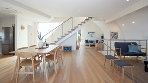 A spacious living area with a wooden dining table, a sofa, and a staircase leading to another level. - Gordons Bay Vista (Clovelly)