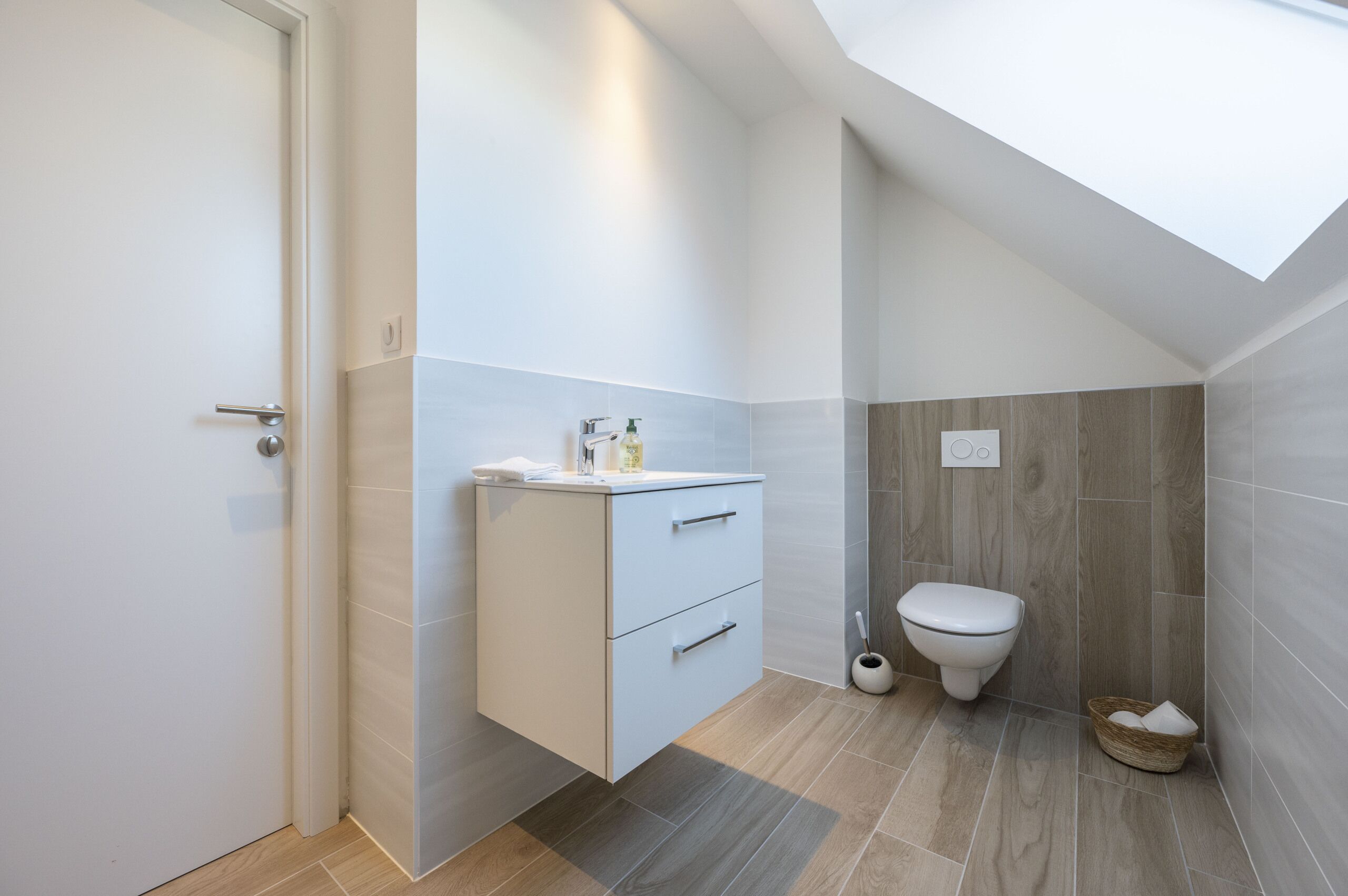 A modern bathroom with a skylight, a toilet, and a cabinet with drawers.