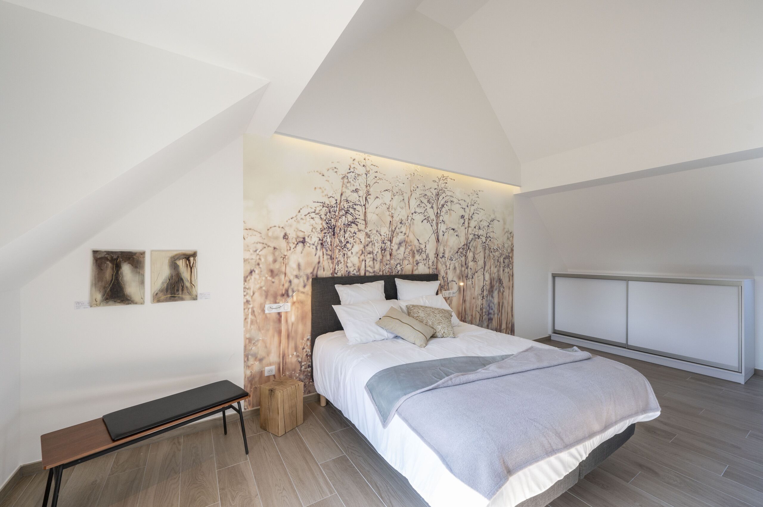 Een slaapkamer met een groot bed, een bankje en een wand met bloemenbehang.