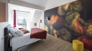 Un dormitorio moderno con una cama, un cuadro grande y una ventana con cortinas rojas.