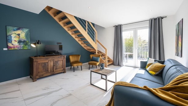 Una sala de estar moderna con una escalera de madera, un sofá, una mesa de centro y un televisor sobre un mueble de madera.