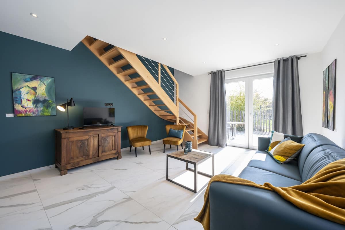 Ein modernes Wohnzimmer mit einer Holztreppe, einem Sofa, einem Couchtisch und einem Fernseher auf einer Holzkommode.