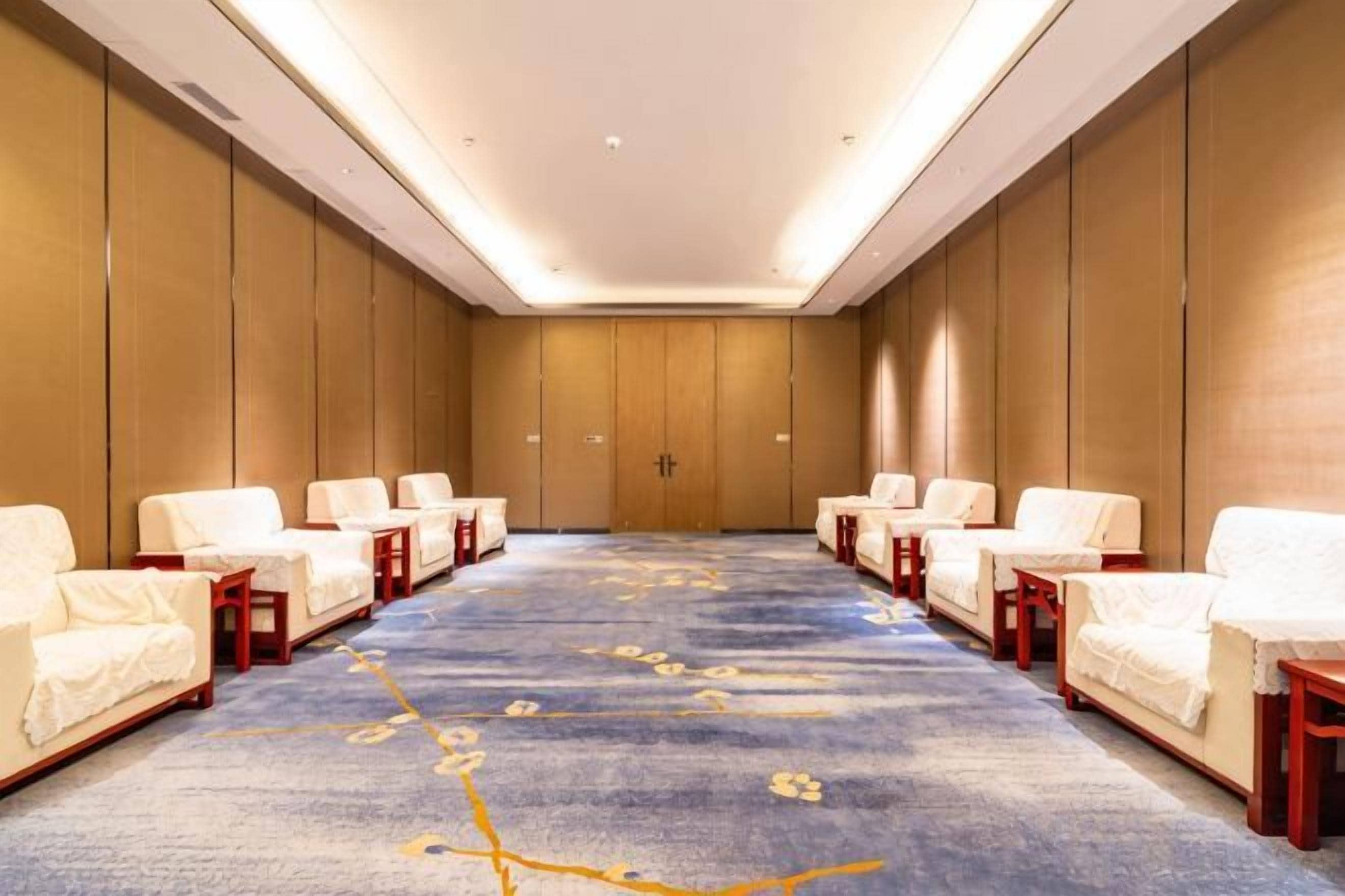 Un salón de conferencias con una mesa larga y varias sillas, piso alfombrado y paneles de madera.