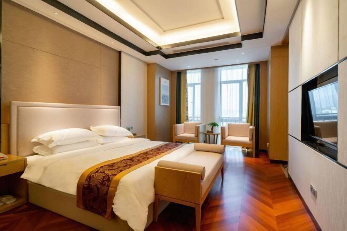 A hotel room with a large bed, a sofa, a TV, and a small table with chairs.