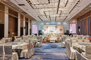 Un salón de banquetes con mesas redondas, sillas y un escenario decorado con flores.
