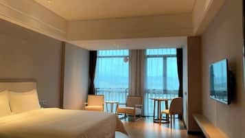 Et hotelværelse med en stor seng, balkon med udsigt, et fjernsyn og et siddeområde med stole og et bord.
