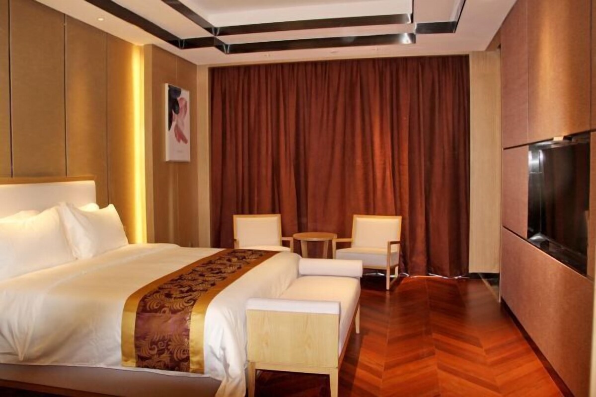 A hotel room with a large bed, two white armchairs, a small table, and a TV.