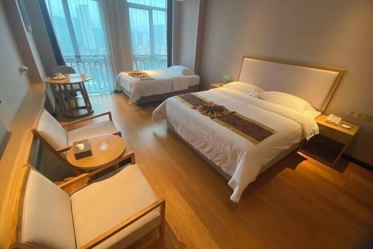 A hotel room with a large bed, a smaller bed, a sofa, a table, and a balcony.