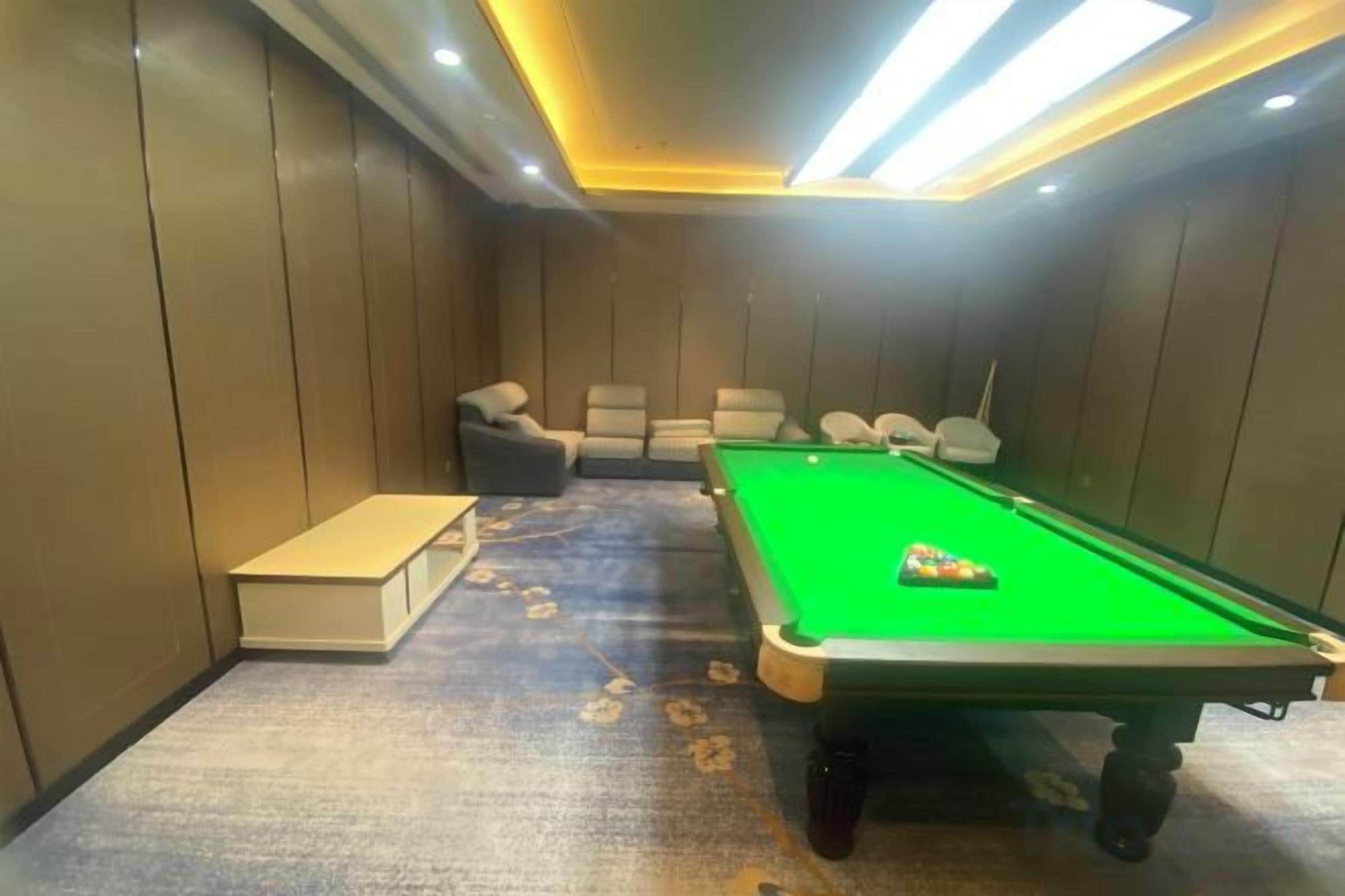 A pool table with a green felt surface, surrounded by four chairs.