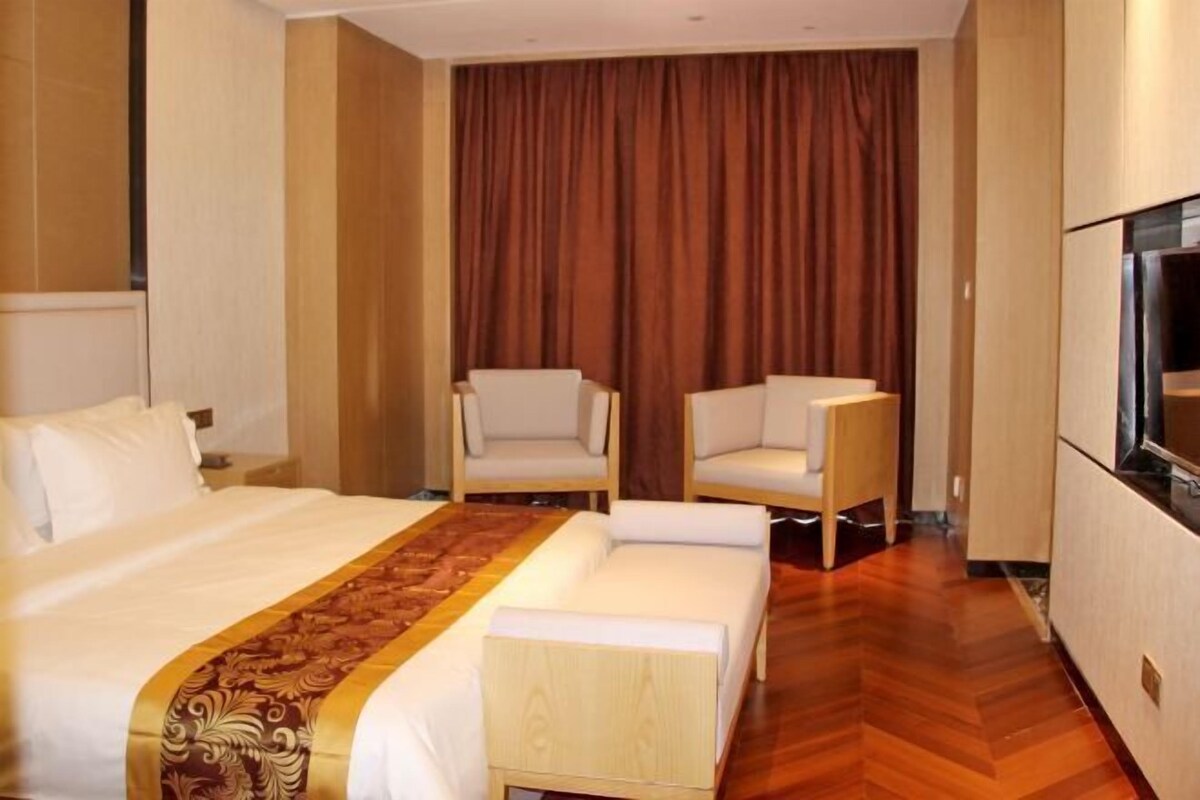 A hotel room with a bed, two chairs, a TV, and a wooden floor.