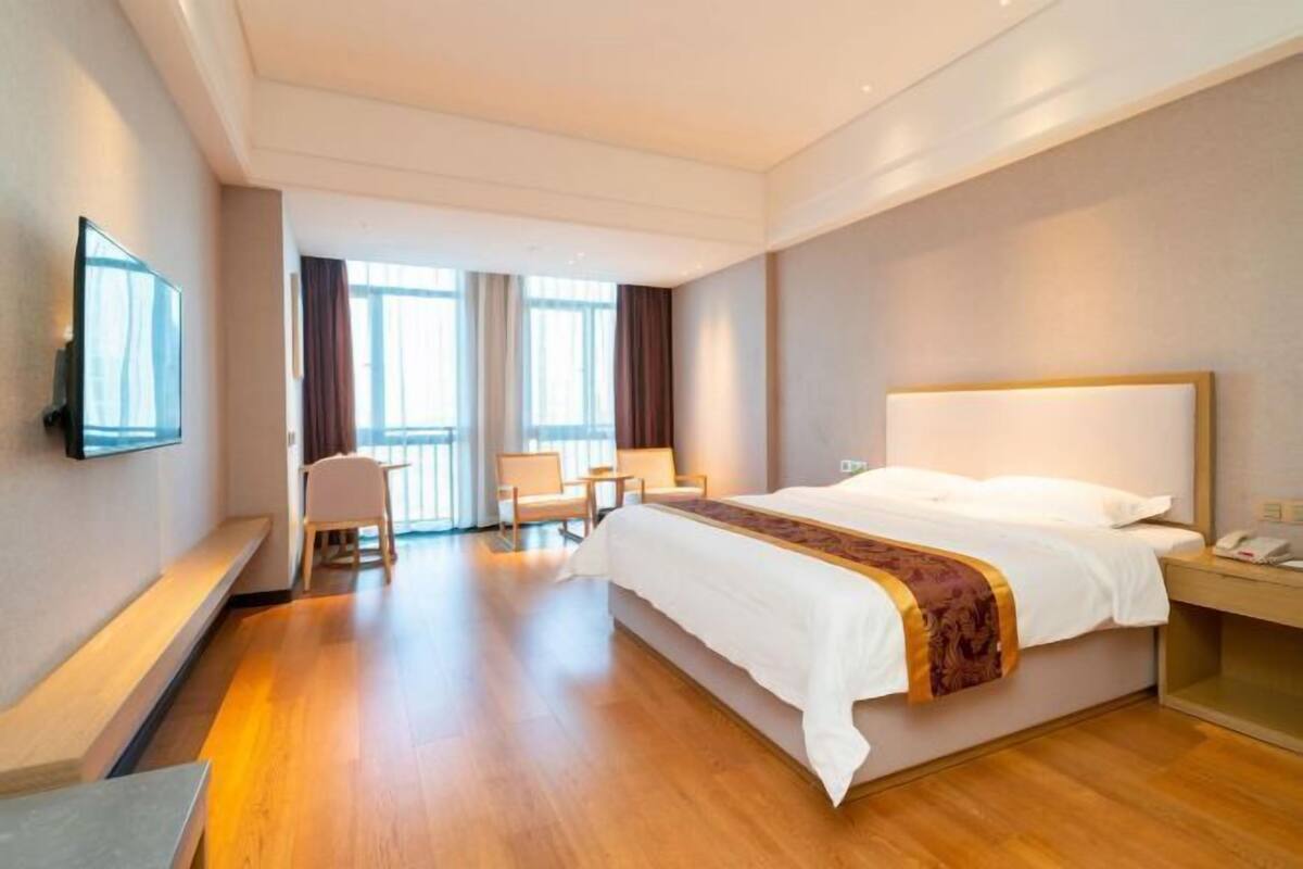 A hotel room with a large bed, a desk, a chair, a TV, and a window with curtains.