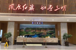 A reception desk with a large painting of a landscape, a sign with Chinese characters, and two potted plants.