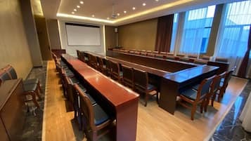 Un salón de conferencias con una larga mesa, sillas, una pantalla de proyector y un amplio ventanal.