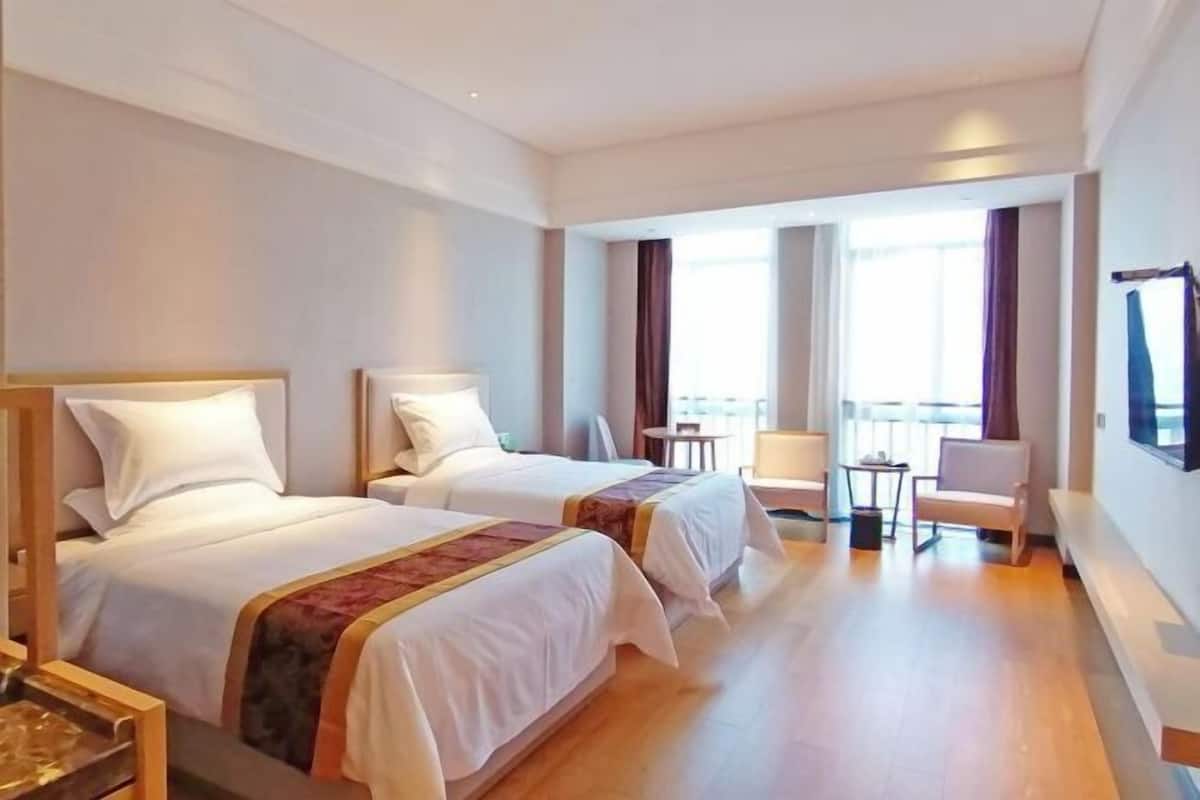 A hotel room with two beds, a small table, a chair, and a window with curtains.