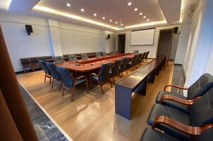 Un salón de conferencias con una larga mesa, sillas y una pantalla para proyector.