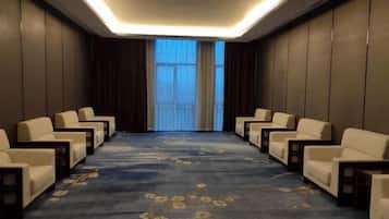 Un salón de conferencias con piso alfombrado, filas de sillas y un gran ventanal con cortinas.