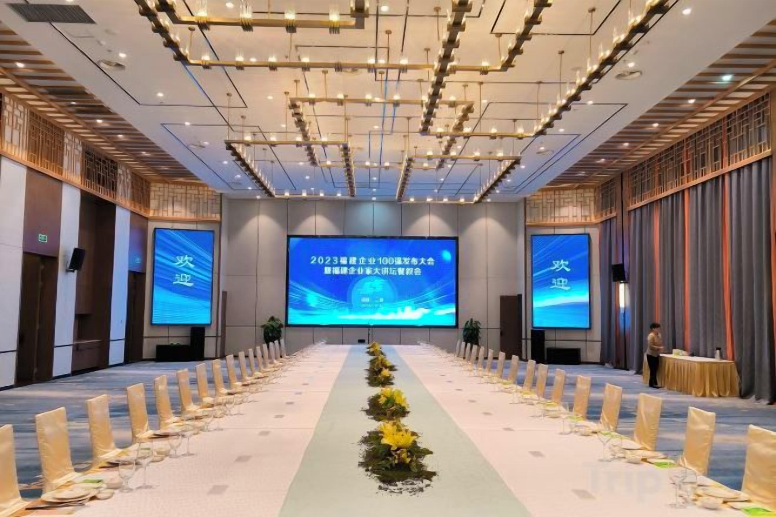 Un salón de conferencias con una larga mesa, pantallas y un orador.
