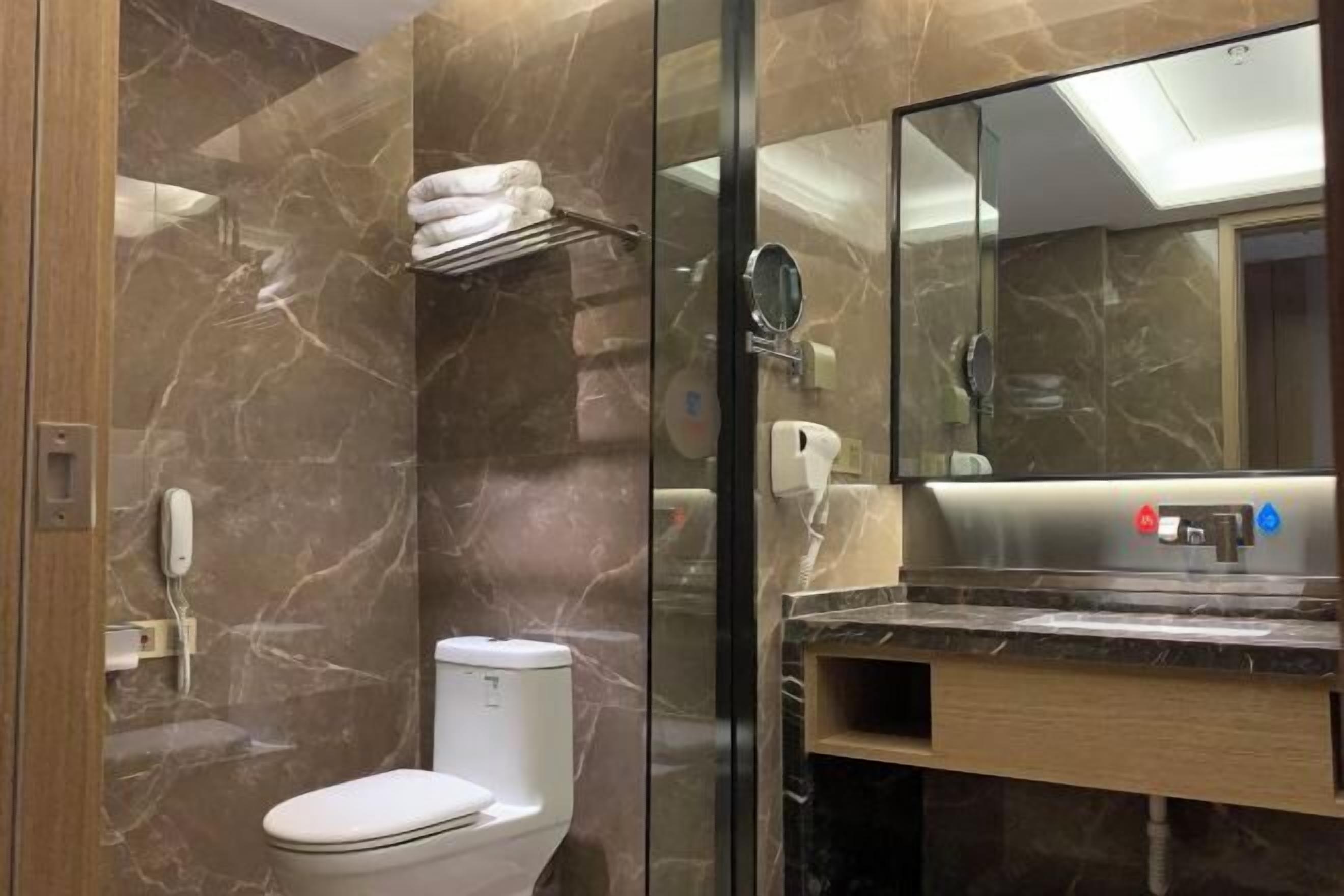 Un baño moderno con pared de mármol, inodoro, lavabo con espejo y perchero para toallas.