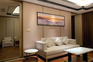 A modern hotel room with a sofa, a small round table, and a painting of a sunset on the wall. - Mingcheng Xincheng Hotel (Sanming)
