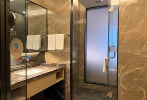 A modern bathroom with a glass shower enclosure, a marble countertop, and a mirror with a towel rack.