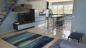 A modern kitchen with a central island, bar stools, and a TV on a cabinet. - Appartement Duplex Bord de mer à Proximité de Tout ! (Saint-François)