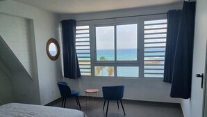A room with a bed, two chairs, a small table, and a large window with curtains. - Appartement Duplex Bord de mer à Proximité de Tout ! (Saint-François)