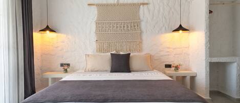 A bedroom with a bed, two bedside tables, a wall-mounted macrame piece, and two pendant lights.
