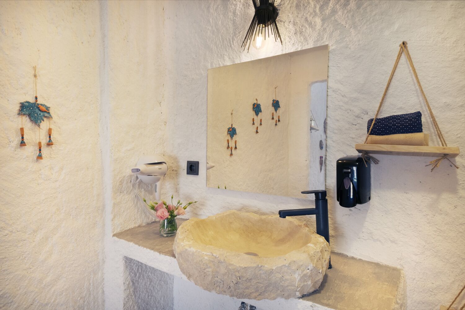 A bathroom with a stone sink, a mirror, a hairdryer, and a hanging ornament.