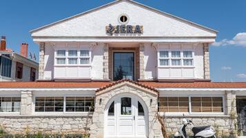Um edifício de dois andares com fachada branca, uma entrada central com porta branca e uma placa acima da porta.