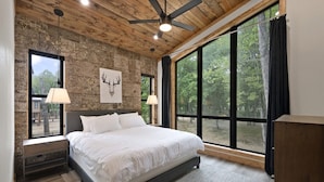Une chambre avec un grand lit, un plafond en bois et une vue sur les arbres, visible à travers de grandes fenêtres.