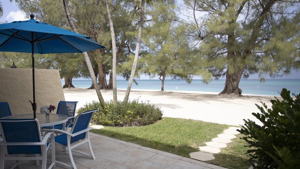 Un patio con una mesa y sillas, una sombrilla azul y vista a la playa y al océano.