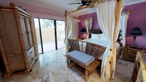 Un dormitorio con cama con dosel, un banco, muebles de mimbre y vistas al exterior.