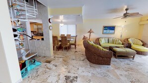 Amplia sala de estar con mobiliario de mimbre, un comedor y una escalera decorada con esculturas de peces.