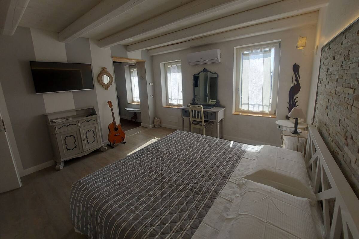 A bedroom with a bed, dresser, guitar, and a television.