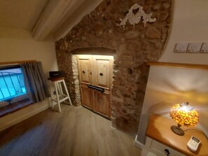 A room with a stone wall, wooden door, and a lamp on a wooden table. - B&B Corte Colli Antichi (Sona)