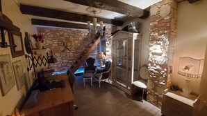 Un interior rústico con paredes de piedra vista, una escalera de madera y un área de descanso con una mesa y sillas.