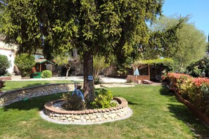 Un jardín bien cuidado con un borde de piedra, un árbol grande y un banco de madera.