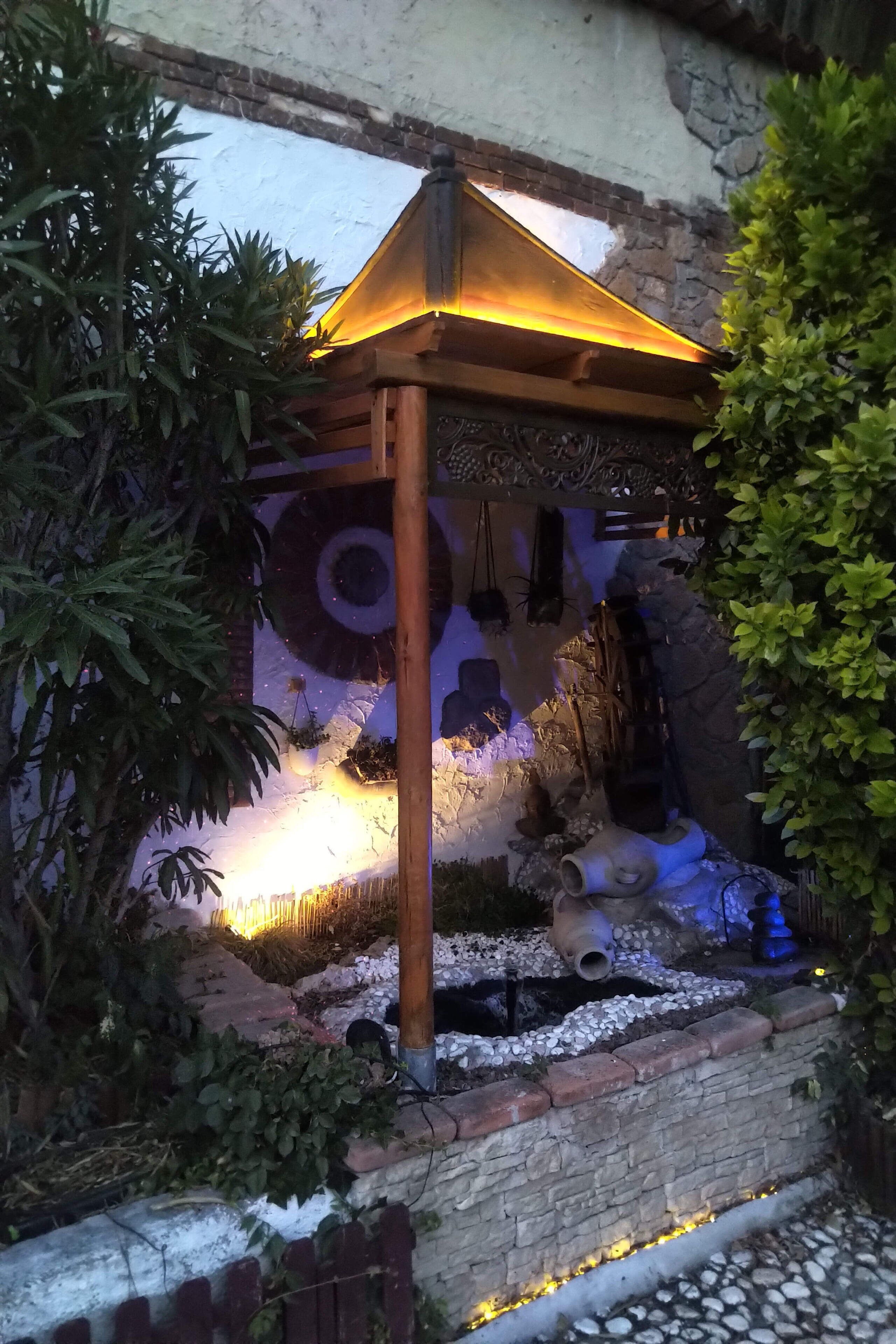 Un espacio al aire libre rústico con una pérgola de madera, muros de piedra y un muro decorativo con motivos circulares.