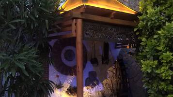 Un espacio al aire libre rústico con una pérgola de madera, muros de piedra y un muro decorativo con motivos circulares.